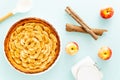 French apple tart aside Gala apples, cooking spoon, white jar, and cinnamon sticks on a light blue background. Flat lay. Top view