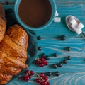 Fresh ruddy croissants with berries lie on a wooden table next to fresh black currant berries, red currants Royalty Free Stock Photo