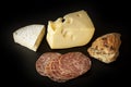 French brie and Swiss Emmental cheese with slices of salami sausage and a home baked bun on black background Royalty Free Stock Photo