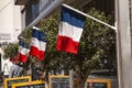 French cafe terrace flies the tri-colors in front of restaurant and shop. Outside image with chairs, tables, billbords and olive t