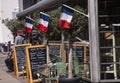 French cafe terrace flies the tri-colors in front of restaurant and shop. Outside image with chairs, tables, billbords and olive t