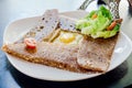 French crepe with chicken slice, cheese, egg on white plate eat with green salad and cherry tomato