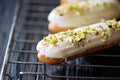 French dessert eclairs or profiteroles with white chocolate glaze with pistachios, on a pastry rack. Pastry cakes with custard, Royalty Free Stock Photo