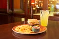 French fries and burger with a knife stuck in the middle- cheese, sausage in a grunge plate,piano with ketchup sauce, with a glass Royalty Free Stock Photo