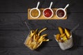 French fries and country potatoes in a basket and three different sauces: Ketchup, Mustard and Barbecue on dark background, top
