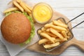 French fries in frying basket, tasty burger and sauce on white wooden table, flat lay