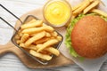 French fries in frying basket, tasty burger and sauce on white wooden table, flat lay