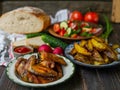 French fries, grilled wings, salad, vegetables, bread on an old wooden background. Rural dinner, summer picnic. Close up