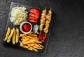 French fries potatoes, chicken skewers, pickles and cabbage, tomatoes and ketchup sauce on black stone background. Hot fast food Royalty Free Stock Photo