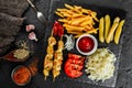 French fries potatoes, chicken skewers, pickles and cabbage, tomatoes and ketchup sauce and spices on black stone background. Hot Royalty Free Stock Photo