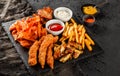 French fries potatoes, grilled meat and fish, chicken nuggets, spicy potato chips, ketchup and mayonnaise on black stone Royalty Free Stock Photo