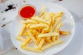 French fries with red tomato sauce on the white plate.