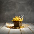 French fries in a small food basket, some scattered on a table. Grey wall background.