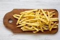 French fries on wooden board over white wooden background, top view.