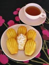 French madeleines and tea in pink vintage dishware on black and magenta cherry-pattern tablecloth