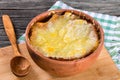 French onion gratin soup in a clay pot, authentic recipe, wooden spoon on a cutting board on an old rustic table, close-up Royalty Free Stock Photo