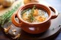french onion soup in a clay dish with thyme sprigs