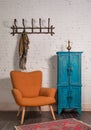 French orange wingback armchair, vintage cupboard, and wall hanger with ornate scarf on bricks wall