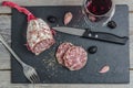 A french saucisson - dry summer sausage on the black background, with a knife, fork, garlic and olives and red wine.