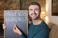 French teacher holding blackboard and French flag. TRANSLATION OF THE TEXT IN THE IMAGE: `Do you speak French?`