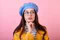 Frenchwoman lady in a stylish hat and beret and a yellow raincoat with glasses shows think on a pink background Royalty Free Stock Photo