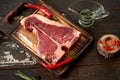 Fresh, aged t-bone steak on a cutting board with two red chili peppers, olive oil, dried tomatoes and paprika on a wooden dark Royalty Free Stock Photo