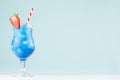 Fresh alcohol blue cocktail with curacao liquor, strawberry slice, ice cubes, red striped straw in misted glass on blue background Royalty Free Stock Photo