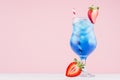 Fresh alcohol blue cocktail with curacao liquor, strawberry slice, ice cubes, red striped straw in misted glass on pink background Royalty Free Stock Photo