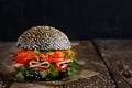 Fresh appetizing bright burger with sesame seeds with fresh vegetables tomato, bell pepper, spicy carrots, parsley and ham, on a