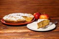 Fresh apples and a piece of apple pie sprinkled with powdered sugar on the background of a dark board.