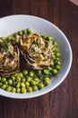 Fresh artichokes with parsley and young beans in a baking pan, parmesan in background.