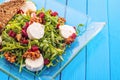 Fresh arugula salad with beetroot, goat cheese, bread slices and walnuts on glass plate on blue wooden background, product