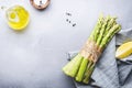 Fresh asparagus bunch, salt, pepper, lemon and olive oil on gray stone kitchen table background, top view, copy space