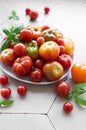 Fresh assorted tomatoes arranged on a white plate with green basil leaves in a bright kitchen setting Royalty Free Stock Photo