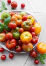 Fresh assorted tomatoes arranged on a white plate with green basil leaves in a bright kitchen setting Royalty Free Stock Photo