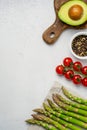 Fresh avocado on cutting board, green asparagus on napkin, cherry tomatoes and pepper mix on grey background. Royalty Free Stock Photo