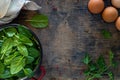 Fresh baby spinach leaves in a bowl and eggs on a wooden table. Top view.