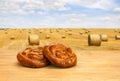 Fresh baked bread on wooden table on a background field with straw bales after harvest