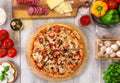 Fresh baked pepperoni pizza on wooden board and table, with colorful ingredients, overhead top view Royalty Free Stock Photo