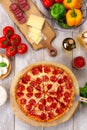 Fresh baked pepperoni pizza on wooden board and table, with colorful ingredients, vertical overhead top view Royalty Free Stock Photo