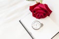 Fresh beautiful red rose with vintage watch on blank white notebook on white bed sheet background Royalty Free Stock Photo