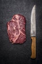 Fresh beef steak with carving knives on dark rustic background top view