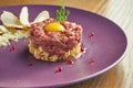 Fresh beef steak tartare with parmesan cheese, capers, croutons and yolk quail on a purple plate on a wooden background