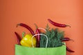 Fresh bell peppers in yellow colors, chili peppers and dill greens in a paper bag on an orange background. Bag for shopping Royalty Free Stock Photo