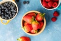 Fresh berries. Blueberry, raspberry and strawberry in colourful bowls. Blue background, top view.