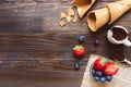 Fresh berries, waffle cone and chocolate sauce on the wooden background, top view. Ice-cream background with copy space