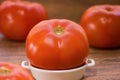 A fresh big red tomato on a white ceramic plate and more tomatoes in background