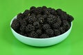 Fresh blackberry in plactic bowl on geen background