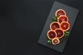 Fresh blood orange slices decorated mint leaves on dark slate background. Top view. Copy space