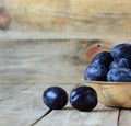 Fresh blue plums with drops of water in a wooden bowl on a wooden background Royalty Free Stock Photo